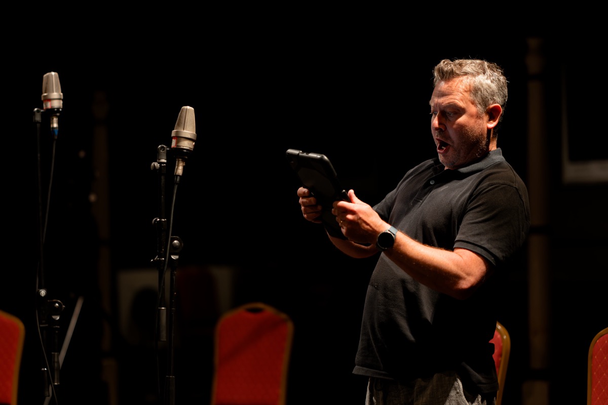 Conductor checking a tablet in front of microphones at a rehearsal