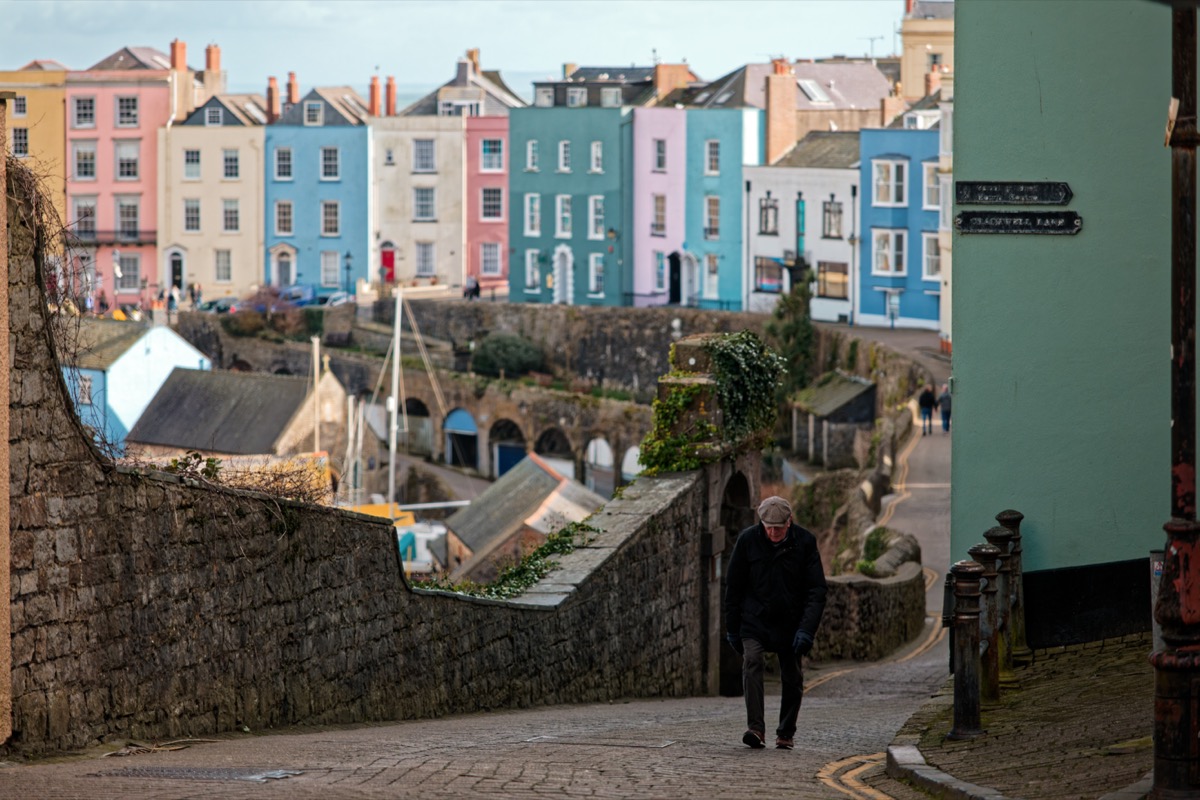 Man walking down a cobbled lane with colourful houses, Tenby harbour